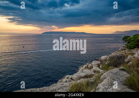 Bateau à moteur naviguant près de la côte dans la Riviera de Makarska à la tombée de la nuit Banque D'Images