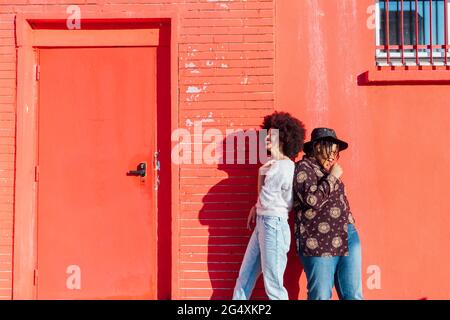 Des amies souriantes se tenant dos à dos près du bâtiment rouge Banque D'Images