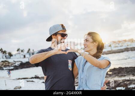 Couple souriant faisant le coeur avec les mains à la plage Banque D'Images