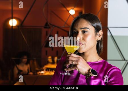 Une jeune femme boit un cocktail tout en regardant loin dans le restaurant Banque D'Images