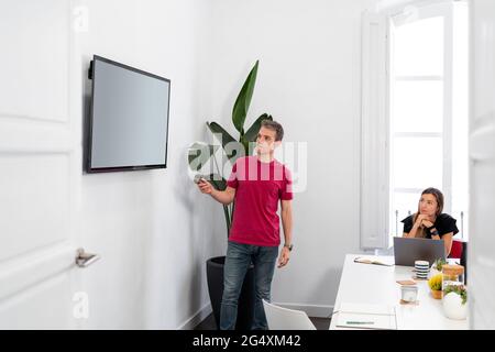 Homme d'affaires conduisant une réunion sur écran de projection dans un bureau de collègue Banque D'Images