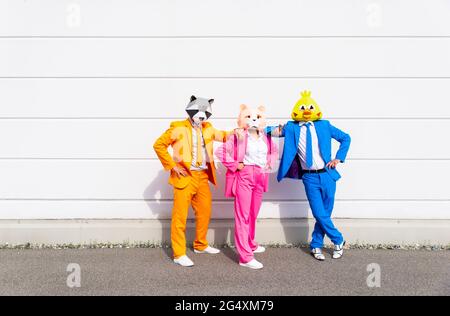 Trois personnes portant des costumes vibrants et des masques pour animaux posant côte à côte devant un mur blanc Banque D'Images