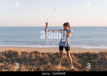 Archeress visant avec l'arc et la flèche tout en se tenant sur l'herbe à la plage Banque D'Images