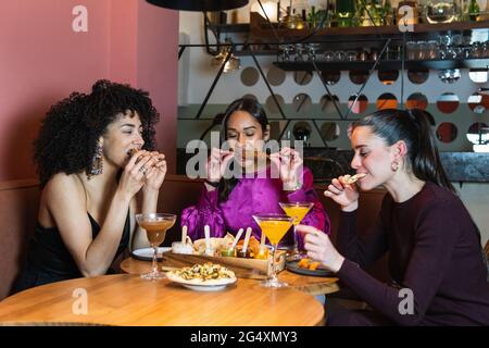 De jeunes amis mangent de la nourriture pendant qu'ils sont assis au restaurant Banque D'Images