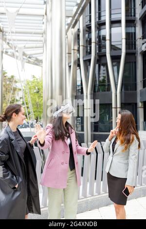 Femme d'affaires qui s'étire la main tout en utilisant un casque de réalité virtuelle par un collègue Banque D'Images