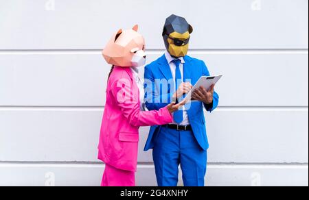 Homme et femme portant des costumes éclatants et des masques pour animaux qui parlent au-dessus du presse-papiers devant le mur blanc Banque D'Images