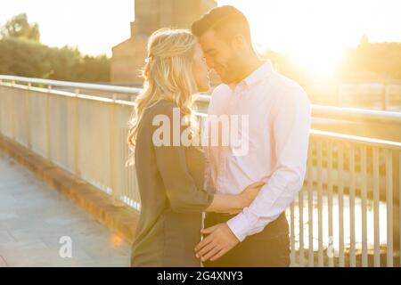 Couple souriant embrassant près des balustrades au coucher du soleil Banque D'Images