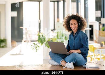 Femme représentant du service clientèle avec un ordinateur portable souriant tout en regardant la cafétéria Banque D'Images