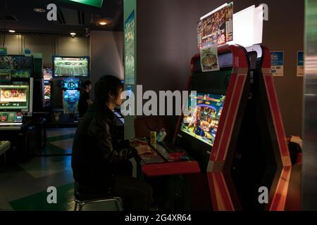 Une personne qui fume tout en jouant à des jeux vidéo dans une arcade japonaise Banque D'Images