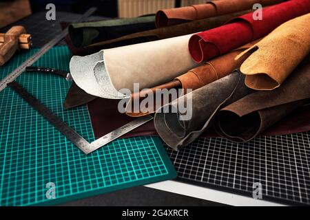 Des échantillons de cuir véritable de différentes couleurs sur une table d'artisanat, entourés d'outils dans un atelier de dressage et de transformation du cuir Banque D'Images