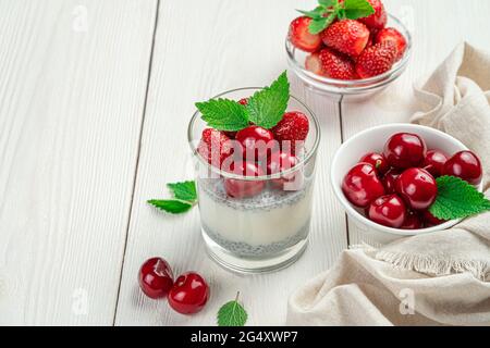 Dessert au lait avec graines de chia, cerises fraîches et fraises. Pouding crémeux sur fond blanc. Banque D'Images
