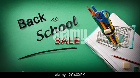 Retour à l'école solde avec panier plein de fournitures sur bloc-notes sur fond vert avec texte. Vue de dessus. Banque D'Images