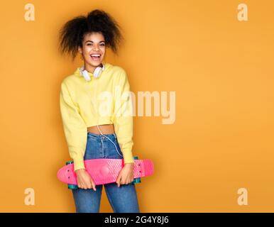 Jeune fille dans un casque tenant une longue planche sur fond jaune Banque D'Images