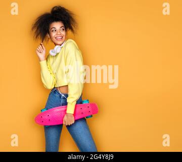 Jeune fille dans un casque avec planche à roulettes regardant de côté sur fond jaune Banque D'Images