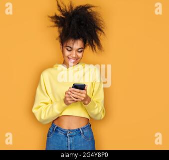 La fille utilise le téléphone, recherche un nouveau message. Photo d'une fille afro-américaine sur fond jaune Banque D'Images