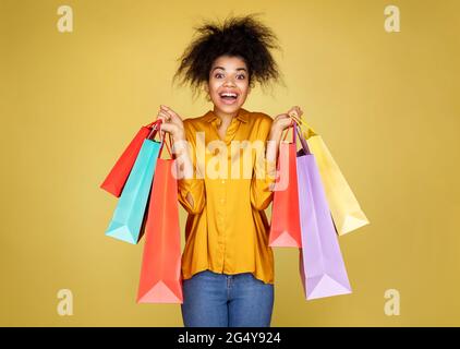 Belle fille heureuse tient des sacs de shopping. Photo d'une fille afro-américaine sur fond jaune Banque D'Images