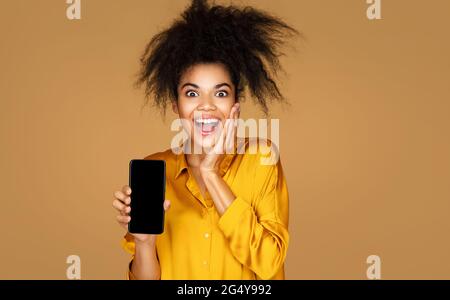 Une fille pleine de joie montre un smartphone à écran. Photo d'une fille afro-américaine sur fond beige Banque D'Images