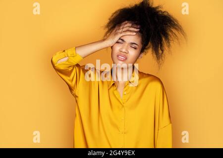 Une fille fatiguée tient la main sur le front étant déprimé. Photo d'une fille afro-américaine sur fond jaune Banque D'Images