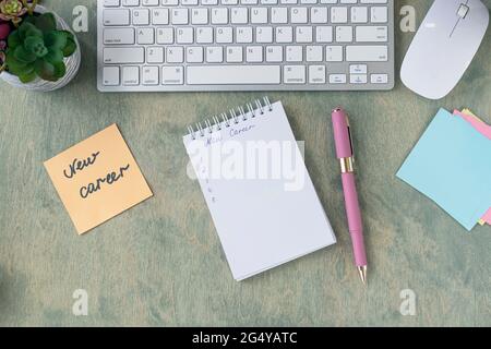 Vue de dessus du bureau avec note avec mots NOUVELLE CARRIÈRE, bloc-notes vide, stylo, clavier, cactus et pause sur une table en bois. Concept commercial et financier. Pose à plat Banque D'Images