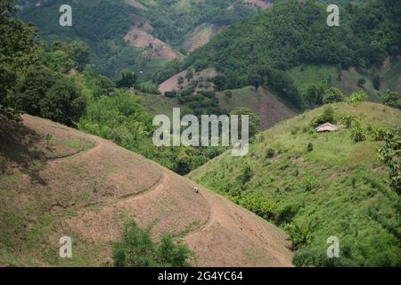 Un paysan s'occupe de sa terre sur une pente de colline massive, dans une vue de sa maison et de nombreuses collines derrière Banque D'Images