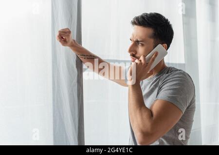 Vue latérale d'un homme concentré parlant sur un téléphone portable près de la fenêtre Banque D'Images