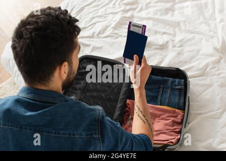 Vue aérienne de l'homme qui tient un passeport avec des billets d'avion près de la valise à la maison Banque D'Images