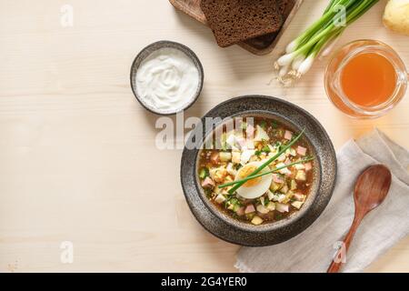 Soupe froide russe d'été Okroshka avec kvass, légumes crus hachés et ingrédients sur fond de bois clair. Vue de dessus. Station santé Copy Banque D'Images