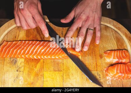 Le chef coupe des filets de saumon pour les sushis sur la planche à découper en bois Banque D'Images