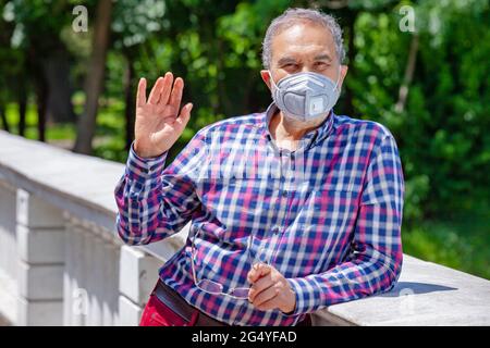 Des hommes âgés avec des vêtements décontractés dans le parc au printemps ou en été, portant un masque de protection du visage agite à la caméra. Banque D'Images