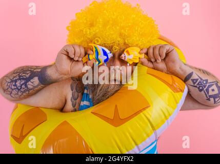 Gros homme avec perruque dans la tête est prêt à nager avec un donut sauvetage Banque D'Images