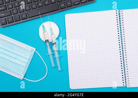 Concept de vaccination, d'immunologie ou de revaccination - deux seringues médicales se trouvant sur une table bleue dans le cabinet du médecin d'un hôpital ou d'une clinique. Ouvert Bloc-notes vide - maquette avec espace de copie Banque D'Images