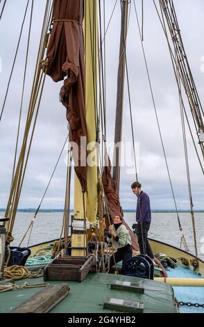 Apprendre les cordes: Deux passagers sur la barge 'Edith May' aidant le skipper Ed Gransden à lever une voile sur un voyage dans l'estuaire de la Tamise, Kent, Angleterre. Banque D'Images