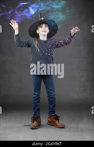 Une petite fille portant un chapeau allowen regarde la fumée colorée. Enfant pour Halloween. Banque D'Images