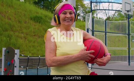 Femme âgée grand-mère après un entraînement sportif de basket-ball assis écoutant de la musique sur le terrain de jeu Banque D'Images