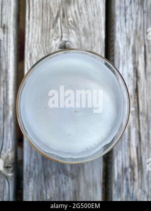 Un verre plat de bière vu d'en haut sur une table en bois dans le jardin de bière. En regardant vers le bas sur la mousse. Banque D'Images