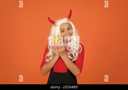 happy kid avec long perruque cheveux porter des cornes diable tenir potiron légume making jack o lanterne pour les fêtes d'automne, halloween Banque D'Images