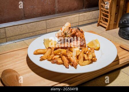 Poulet grillé maison servi sur une assiette blanche en céramique avec des pommes de terre frites rustiques et de la sauce. Isolé sur panneau en bois. Banque D'Images