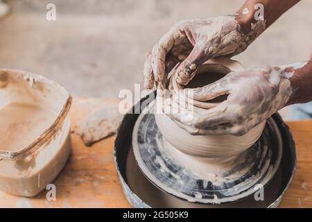 gros plan sur les mains africaines américaines sculptant le pot d'argile sur la roue en poterie Banque D'Images