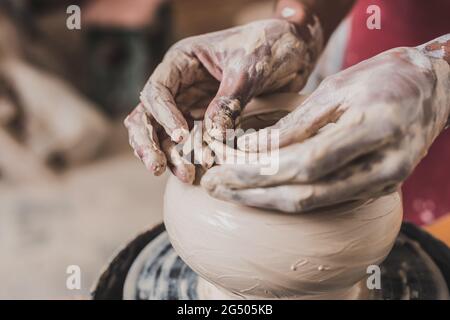 vue rapprochée des mains mâles afro-américaines sculptant la terre battue sur la roue en poterie Banque D'Images