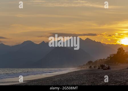 Belle photo des gens qui marchent sur la plage de Konyaalti à Antalya, sur fond du ciel de coucher de soleil Banque D'Images