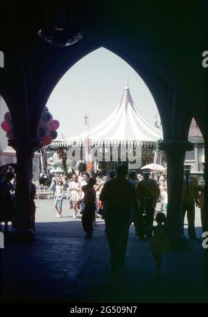 Disneyland, Californie, 1959. Une scène animée montrant une vue sur le roi Arthur carrousel depuis le château de Sleeping Beauty, Fantasyland. Les visiteurs passent et un vendeur de ballons et les musiciens de Disneyland sont au premier plan. Banque D'Images