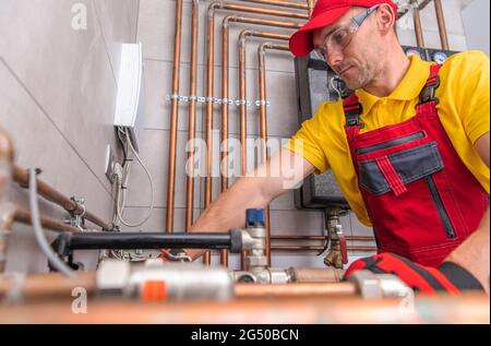 Technicien de systèmes de chauffage résidentiels de Caucasiens dans ses années 40 au travail. Eau chaude et froide canalisations en cuivre en arrière-plan. Banque D'Images