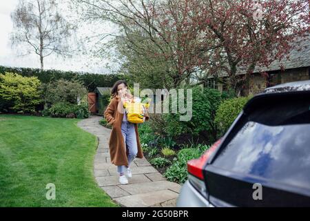 Une jeune femme transportant des articles d'épicerie à sa voiture dans un sac à provisions réutilisable. Banque D'Images