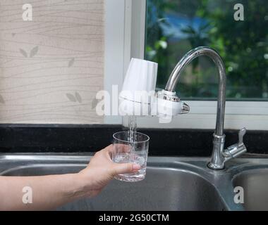 femme versant de l'eau dans le verre du filtre à eau de la cuisine. Verser de la boisson fraîche propre. Banque D'Images