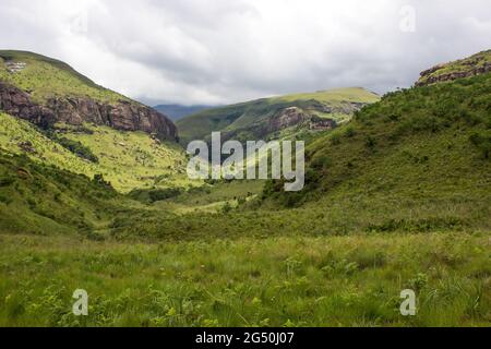 Une vallée entourée par les pentes couvertes d'herbe des montagnes du Drakensberg, en Afrique du Sud, avec des nuages de tempête se rassemblant au loin Banque D'Images