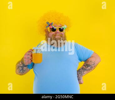 Gras Happy man avec perruque dans la tête et lunettes de soleil boit un jus de fruit Banque D'Images