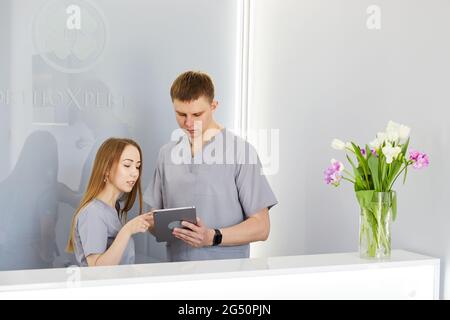 Dentiste avec infirmière dentaire dans un cabinet dentaire moderne utilisant un PC tablette portant l'uniforme. Spécialiste en orthodontie et assisant à la réception en clinique dentaire d Banque D'Images