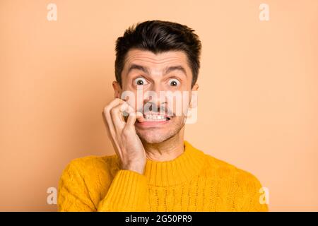 Photo portrait d'un homme nerveux stupéfié, avec ses doigts mordus, isolé sur fond beige pastel Banque D'Images