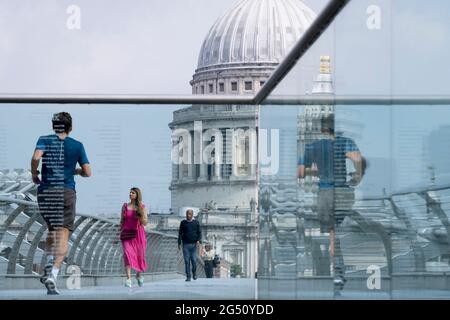 Avec le dôme de la cathédrale Saint-Paul au loin, une femme vêtue d'une robe pourpre traverse la Tamise sur le pont du millénaire, le 24 juin 2021, à Londres, en Angleterre. La plus récente traversée de la rivière de Londres depuis plus de 100 ans a coïncidé avec le Millenium. Elle a été achevée à la hâte et ouverte au public le 10 juin 2000, quand environ 100,000 personnes l'ont traversée pour découvrir que la structure oscille tellement qu'elle a été forcée de fermer 2 jours plus tard. Au cours des 18 prochains mois, les concepteurs ont ajouté des amortisseurs pour arrêter sa vacillement, mais il symbolisait déjà ce qui était embarrassant et qui ne parvenait pas à la fierté britannique. Maintenant Banque D'Images