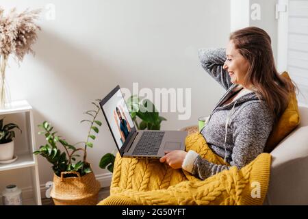 Fille gaie assise dans un fauteuil discutant avec des amis en ligne Banque D'Images